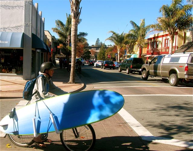 California kid on  a bike with surfboard in beachtown on the ocean